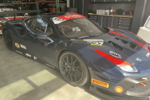 Dark blue Ferrari race car with red accents in a garage, number 397 and sponsor decals visible on the hood and sides.