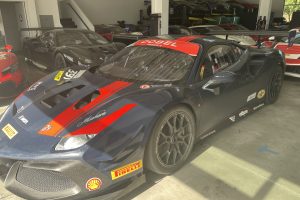Dark blue race Ferrari with red stripes in a showroom, sponsor stickers on sides and hood, indoor garage backdrop