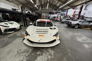 IMG_5387 – Sage Auto Sport White Ferrari race car with Pirelli stickers in a busy automotive workshop, with other sports cars on lifts around it.