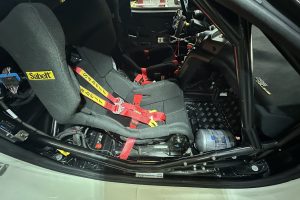 IMG_5390 – Sage Auto Sport Racing car interior with red five-point safety harnesses attached to black bucket seats in a cockpit setting.