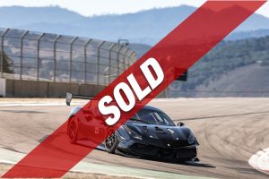 Black Ferrari race car on a curving track with a large red diagonal SOLD banner across the image.