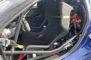 IMG_4766 – Sage Auto Sport Cockpit of a race car with a padded racing seat, Sabelt label on the harness, and a visible roll cage with safety straps in place.