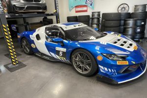 Blue and white race car with number 5 inside a garage full of stacked tires and a car on a lift above.