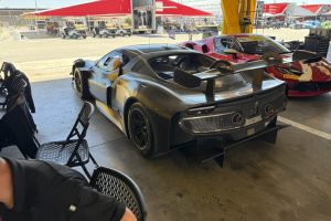 IMG_1574 – Sage Auto Sport Black high-performance race car with a large rear wing in a pit area under red canopies.