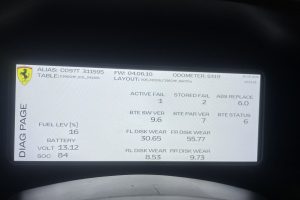 IMG_8599 – Sage Auto Sport Close-up of a car diagnostic screen showing Ferrari logo and numeric readouts (fuel, battery, odometer, faults) on a white background.