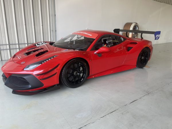 IMG_4471 – Sage Auto Sport Red racing car in a garage with a large carbon fiber rear wing and black wheels, number 26 on the hood.