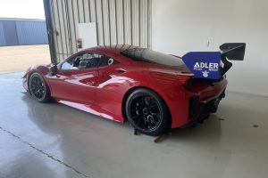 IMG_4472 – Sage Auto Sport Red race car inside a garage, featuring a large blue rear wing with Adler Group branding on the wing endplate.