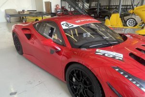 IMG_4475 – Sage Auto Sport Red Ferrari race car in a garage, showing glossy red body, black multi-spoke wheels, and race stickers with number 607.