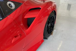 IMG_4487 – Sage Auto Sport Close-up of a red sports car focusing on the front fender vent and black alloy wheel with glossy paint reflections, in a showroom.