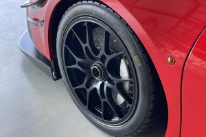 IMG_4488 – Sage Auto Sport Close-up of a red sports car's wheel and fender, showing a dark multi-spoke alloy rim and exposed brake components behind the tire