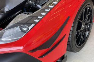 IMG_4489 – Sage Auto Sport Close-up of a red sports car's front section, showing a black front splitter, sleek headlamp, and large black wheel with low-profile tire.
