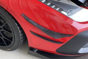 IMG_4492 – Sage Auto Sport Close-up of a red motorcycle nose showing a black front lip, wheel with a dark alloy rim, and a clear windscreen reflecting light.