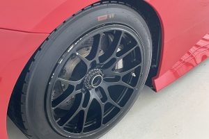 IMG_4494 – Sage Auto Sport Close-up of a red car's wheel with a black alloy rim and low-profile tire, resting on a concrete floor